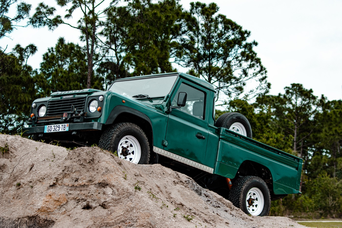 Land Rover Defender 110 pick-up vert en croisement de ponts sur une butte de sable